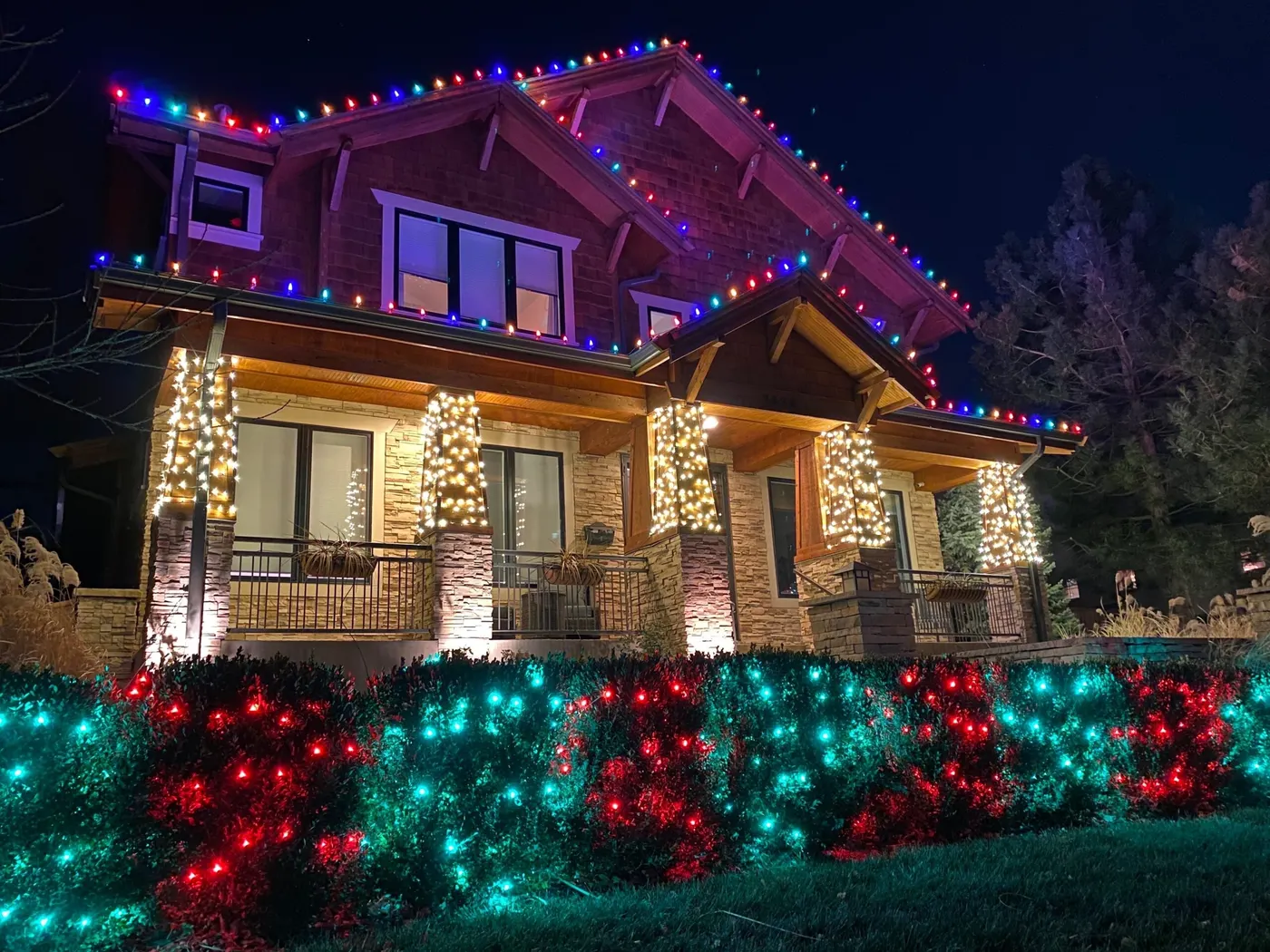 Craftsman home with a multicolor roofline, lit columns, and bushes covered in red and green lights