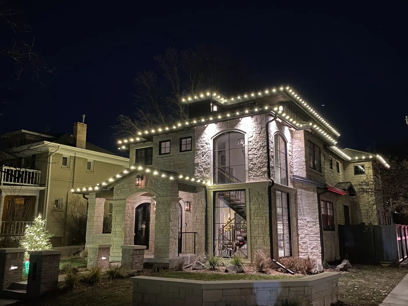 Stone and stucco home with warm white C9 lights tracing every roofline and gable